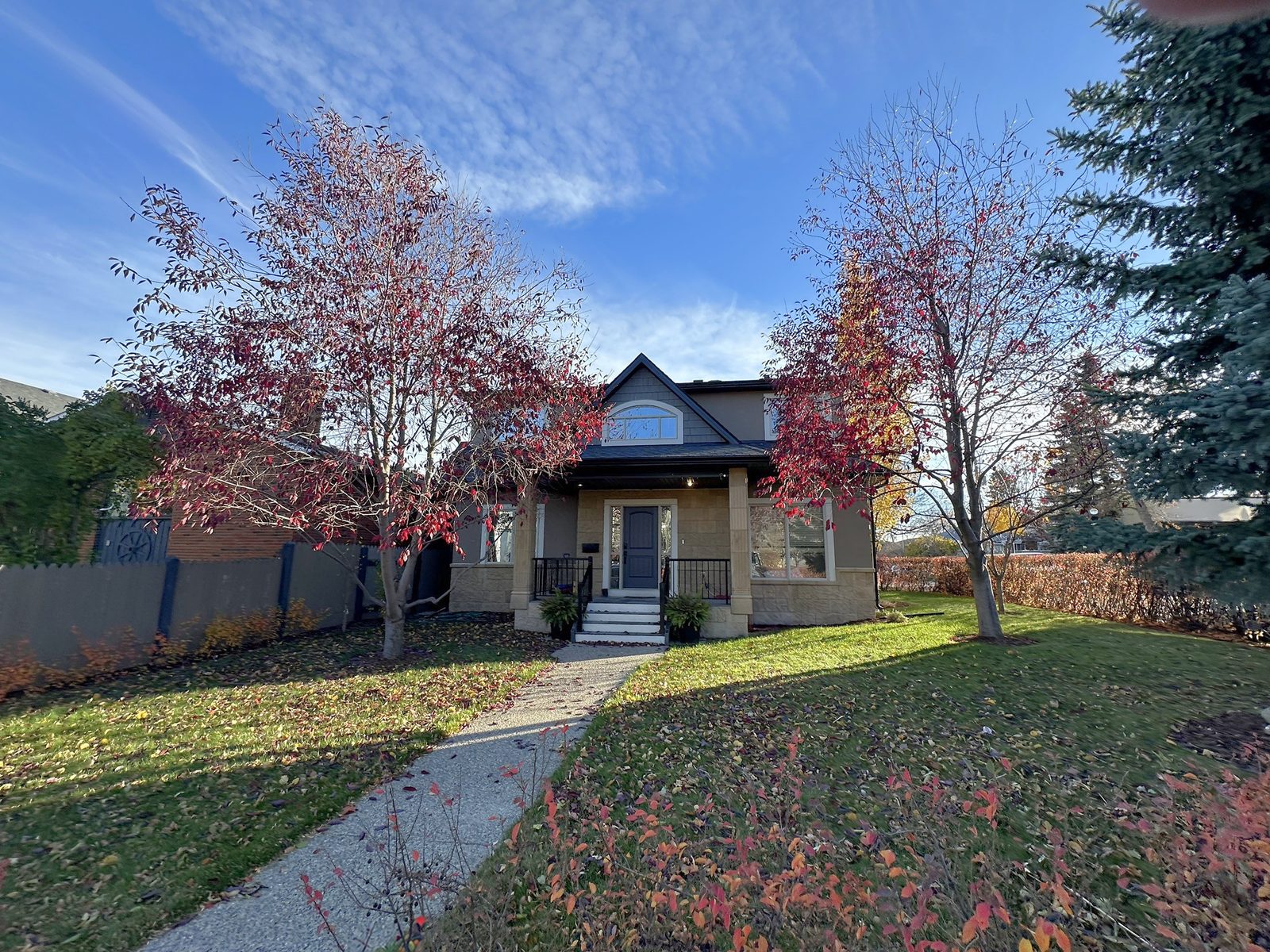 Two-storey stucco and stone home behind red-leafed trees on a corner lot